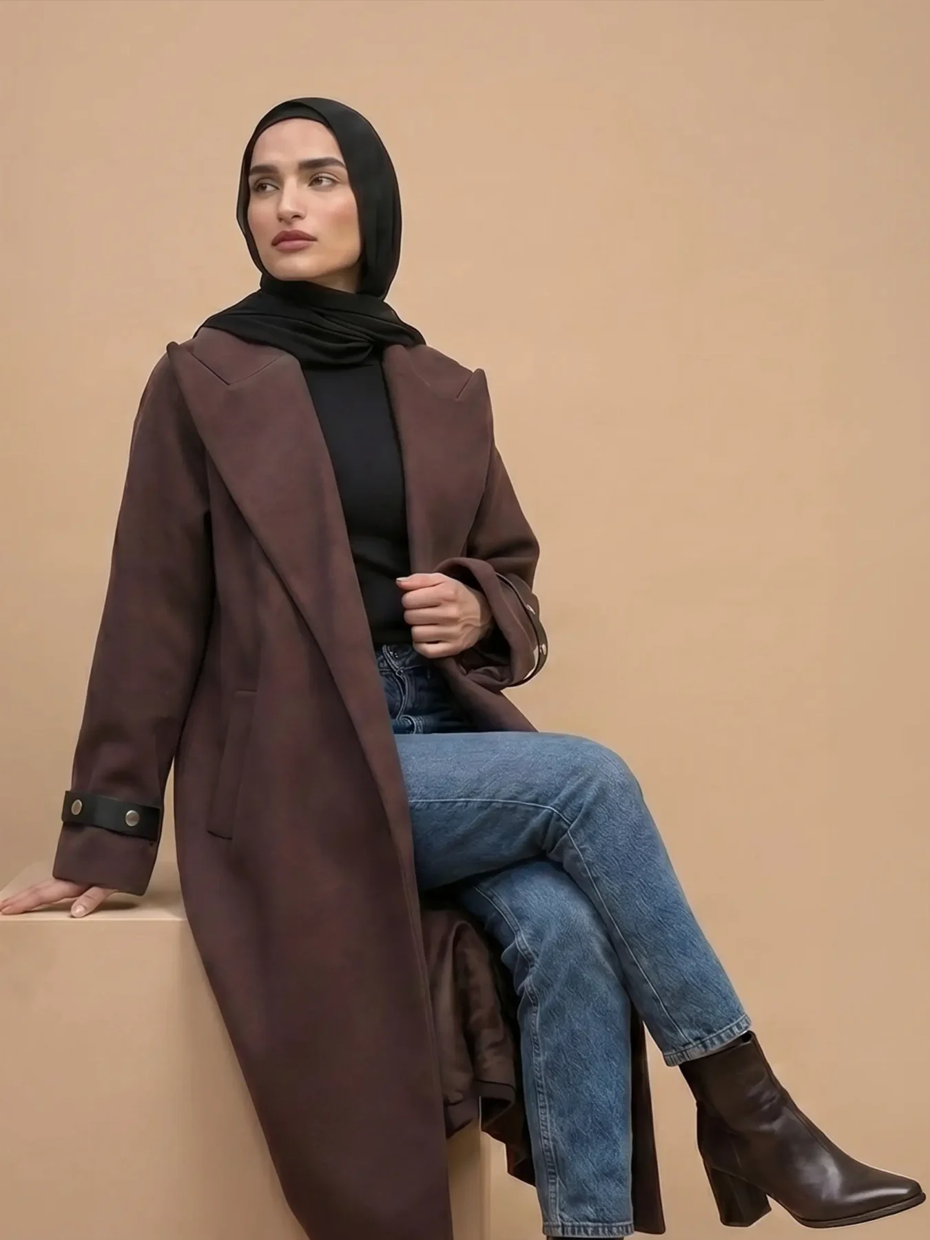 Mannequin en manteau chocolat assise sur un cube beige